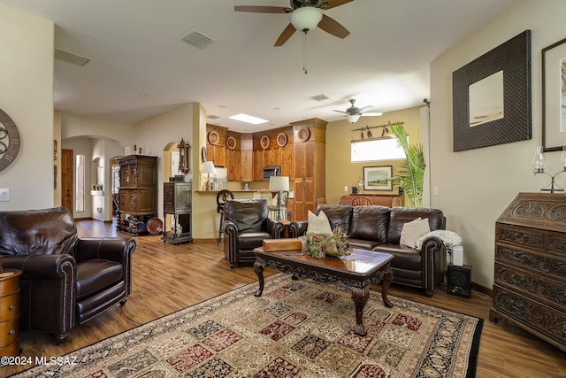 living room featuring wood finished floors, visible vents, arched walkways, and ceiling fan