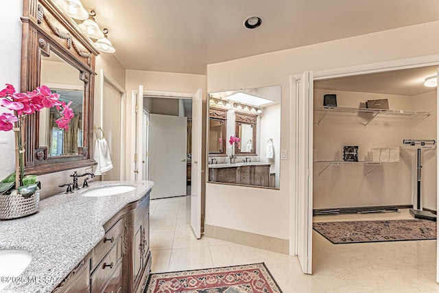 full bathroom featuring baseboards, a sink, a walk in closet, double vanity, and marble finish floor