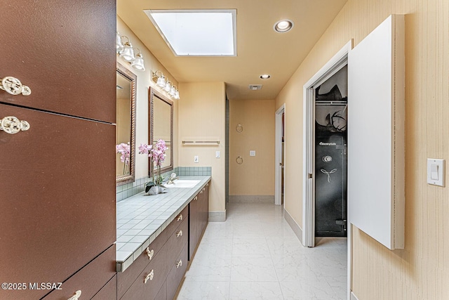 bathroom featuring baseboards, recessed lighting, vanity, a skylight, and marble finish floor