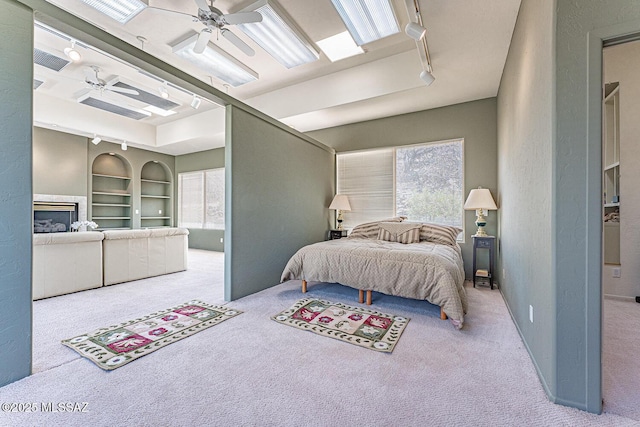 carpeted bedroom with visible vents, ceiling fan, rail lighting, and a glass covered fireplace