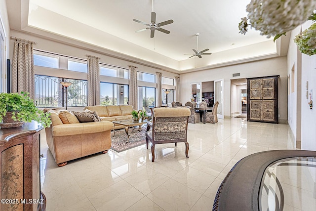 living room with a raised ceiling, marble finish floor, and a ceiling fan