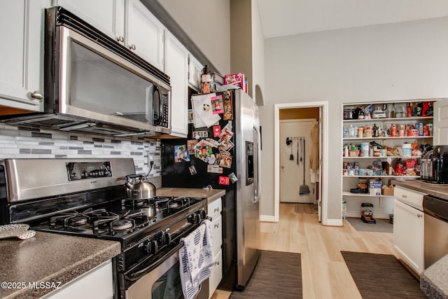 kitchen with tasteful backsplash, stainless steel appliances, dark countertops, light wood-style floors, and white cabinets