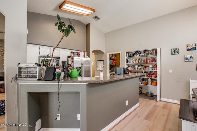 kitchen featuring vaulted ceiling, light wood finished floors, stainless steel fridge with ice dispenser, visible vents, and white cabinets