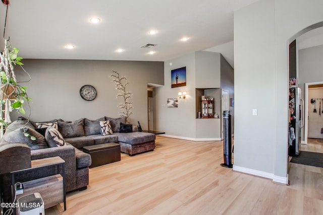 living room featuring vaulted ceiling, baseboards, arched walkways, light wood-style floors, and visible vents