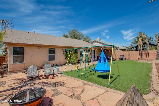 back of house featuring a fire pit, a playground, fence, a patio, and a yard