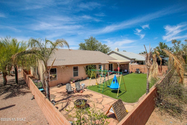 rear view of property with a patio area, stucco siding, a fenced backyard, a lawn, and a playground