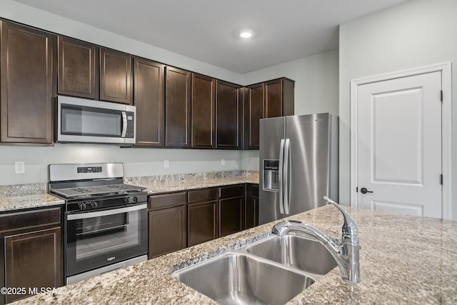 kitchen with dark brown cabinetry, light stone counters, a sink, and stainless steel appliances
