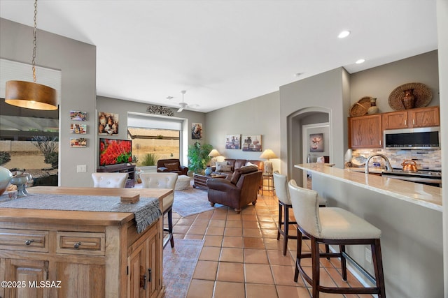kitchen with a breakfast bar, light tile patterned flooring, stainless steel microwave, light countertops, and backsplash