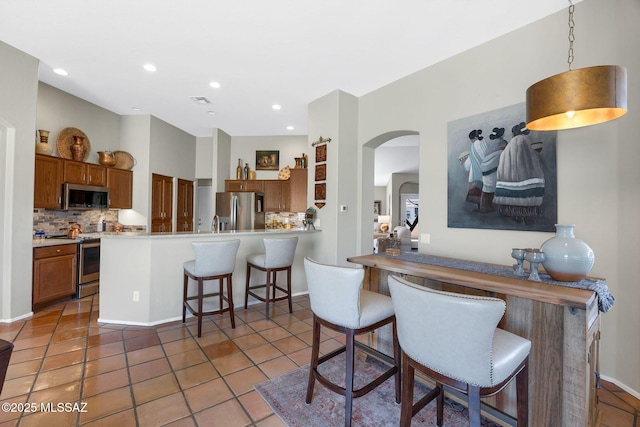 kitchen with stainless steel appliances, tasteful backsplash, arched walkways, and brown cabinets