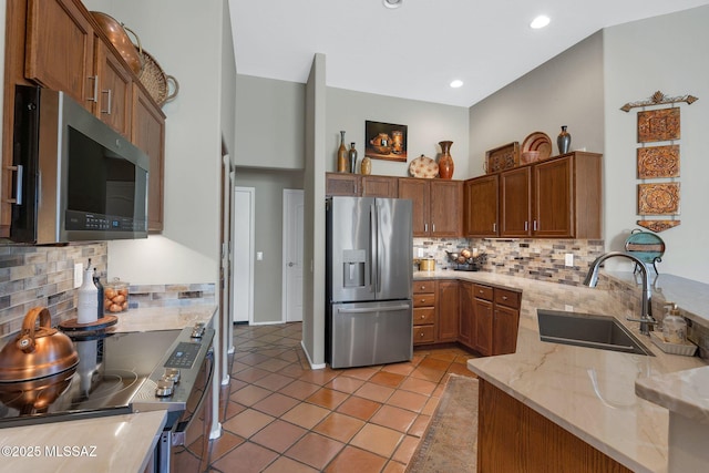 kitchen with tasteful backsplash, a sink, light stone counters, and appliances with stainless steel finishes
