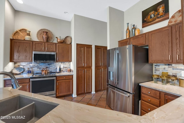 kitchen featuring tasteful backsplash, light stone counters, brown cabinets, stainless steel appliances, and a sink