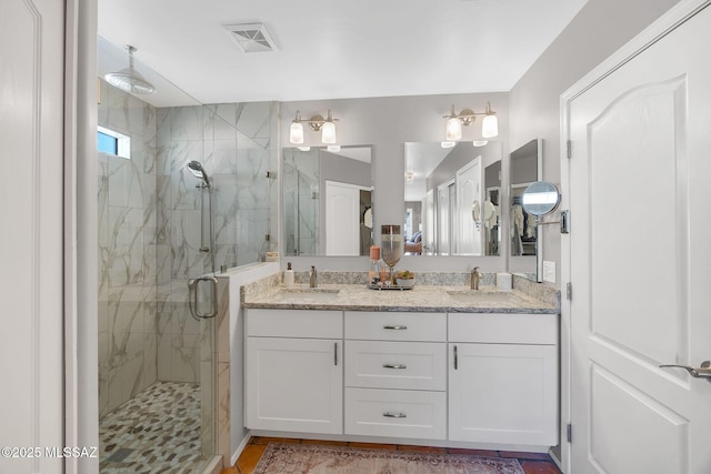 bathroom with a sink, visible vents, a marble finish shower, and double vanity