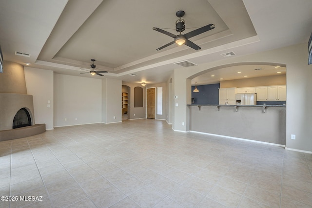 unfurnished living room featuring a tray ceiling, visible vents, a fireplace, and a ceiling fan