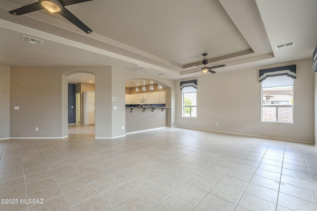 interior space featuring a tray ceiling, visible vents, light tile patterned flooring, and ceiling fan