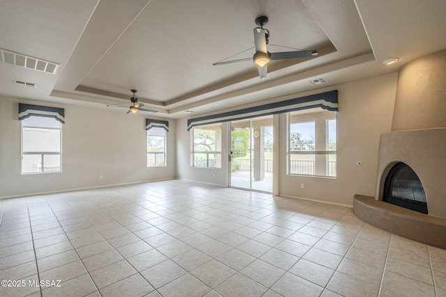 unfurnished living room featuring light tile patterned floors, visible vents, a ceiling fan, and a raised ceiling