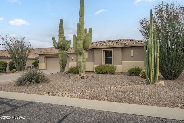 view of front facade featuring a tile roof, driveway, stucco siding, and an attached garage