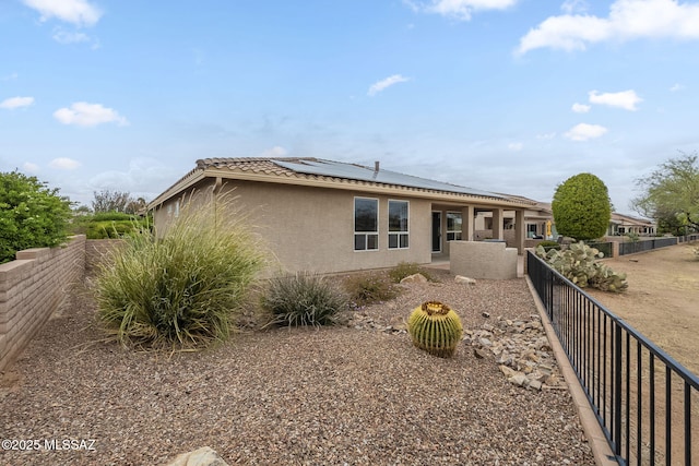 back of house featuring a fenced backyard, solar panels, stucco siding, and a tile roof