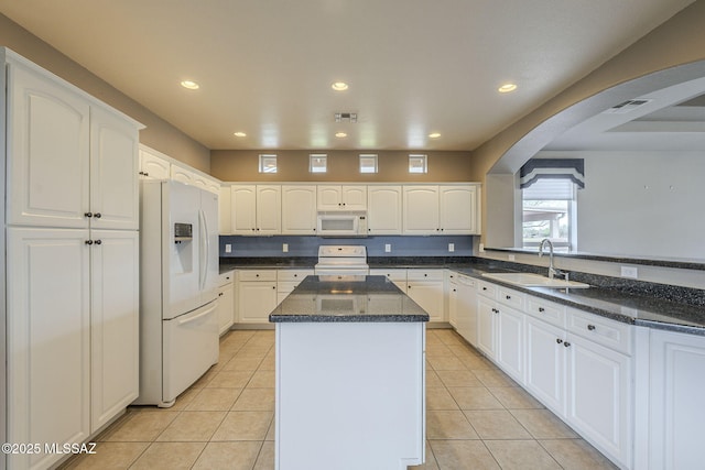 kitchen featuring white appliances, a kitchen island, a sink, arched walkways, and visible vents