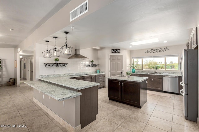 kitchen featuring a sink, wall chimney exhaust hood, a peninsula, stainless steel appliances, and visible vents