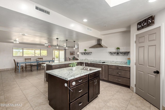 kitchen featuring wall chimney range hood, visible vents, a sink, and dark brown cabinets