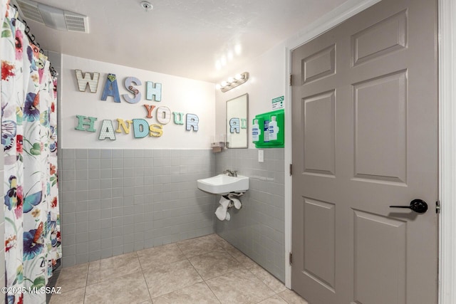 full bath featuring tile patterned floors, a shower with curtain, wainscoting, visible vents, and tile walls