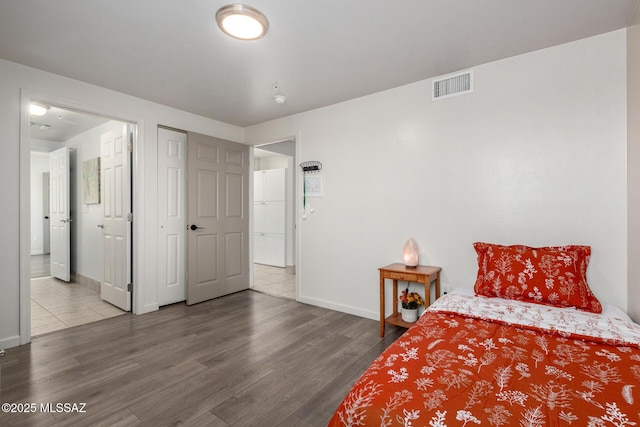 bedroom featuring baseboards, ensuite bath, visible vents, and wood finished floors