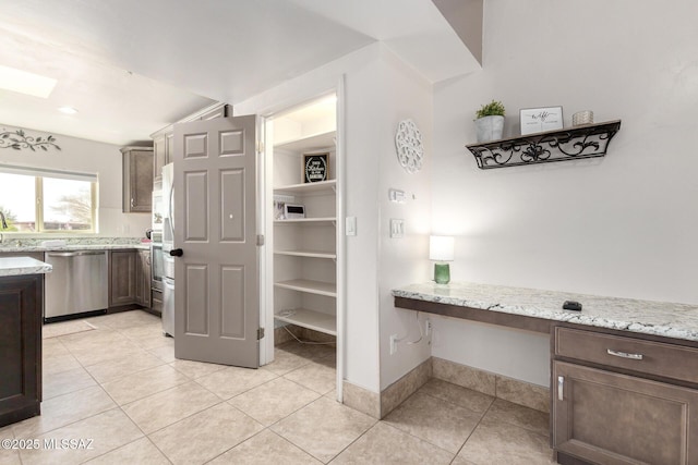 kitchen featuring dishwasher, built in desk, light stone countertops, dark brown cabinetry, and light tile patterned floors