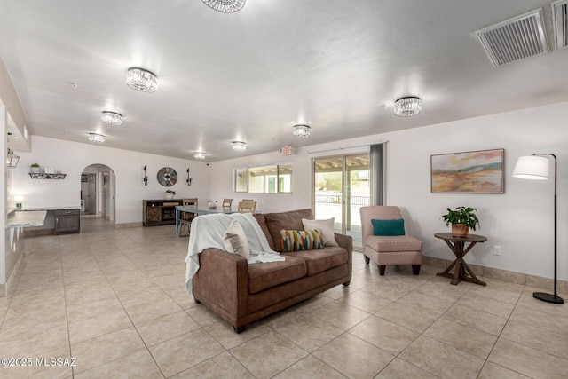 living room featuring light tile patterned floors, arched walkways, baseboards, and visible vents