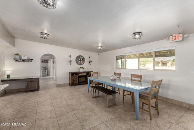 dining area featuring light tile patterned flooring, baseboards, and arched walkways