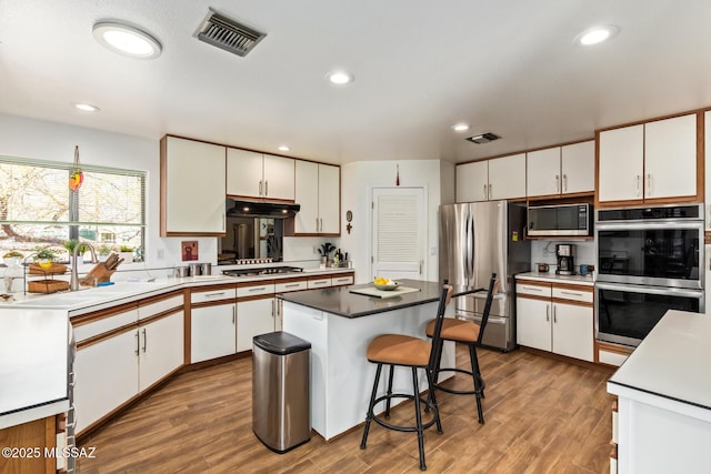 4720 E Wagon Train Rd, Tucson, AZ 85739 - kitchen with white cabinets, visible vents, wood finished floors, appliances with stainless steel finishes, and under cabinet range hood