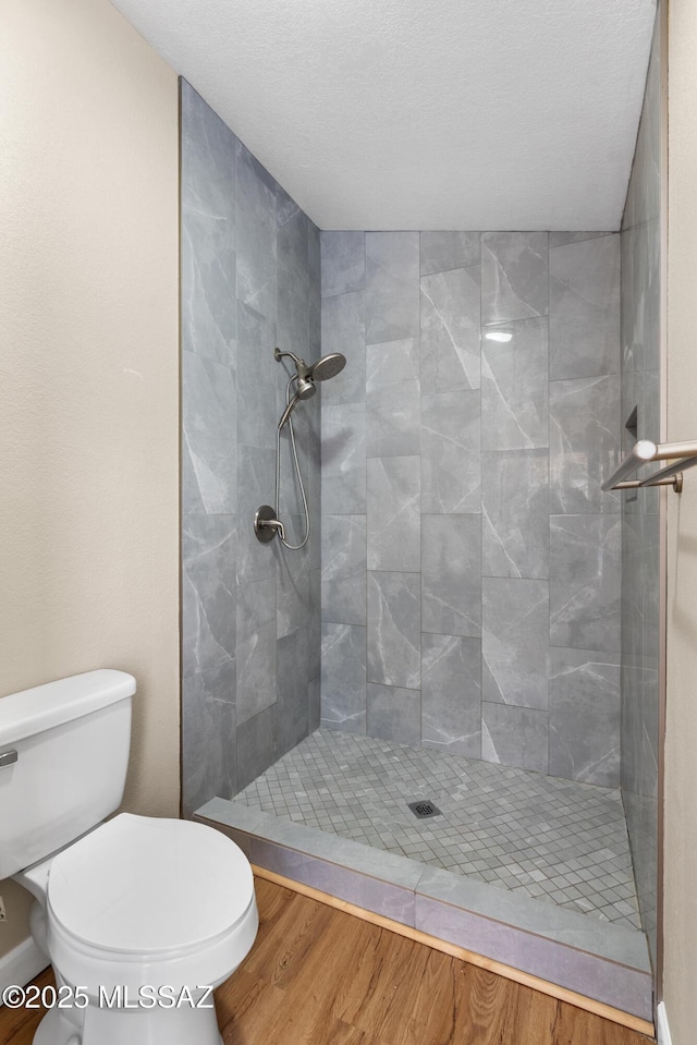 bathroom with toilet, wood finished floors, baseboards, and a tile shower