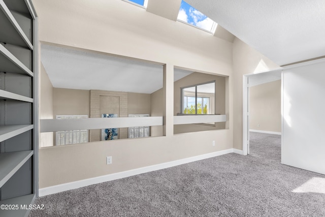 carpeted spare room featuring vaulted ceiling with skylight and baseboards
