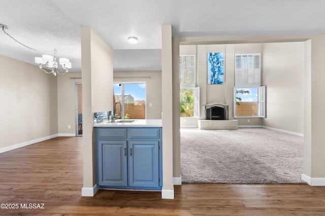unfurnished living room featuring an inviting chandelier, a fireplace, wood finished floors, a sink, and baseboards