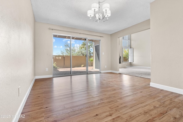 unfurnished dining area with a textured ceiling, wood finished floors, a notable chandelier, and baseboards