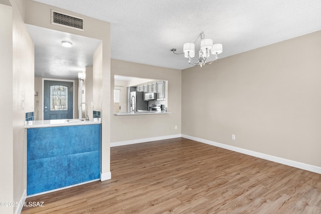 interior space featuring baseboards, a chandelier, visible vents, a sink, and wood finished floors