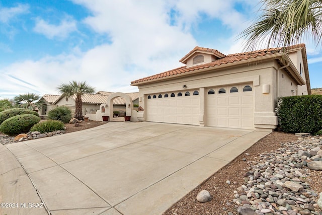 mediterranean / spanish house with a tile roof, stucco siding, a garage, and driveway