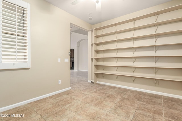 unfurnished room with arched walkways, light tile patterned flooring, baseboards, and a ceiling fan