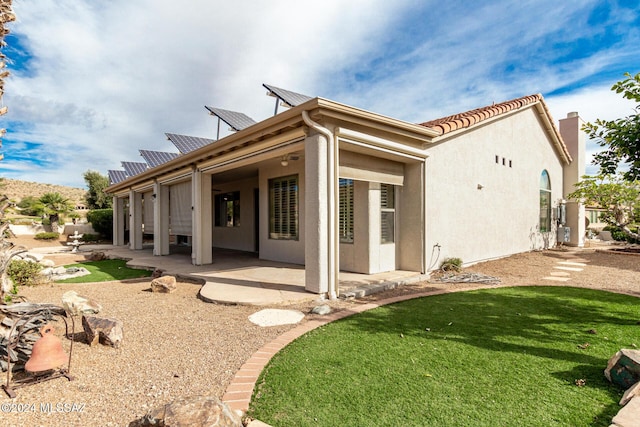 back of property featuring a lawn, stucco siding, a patio, and roof mounted solar panels