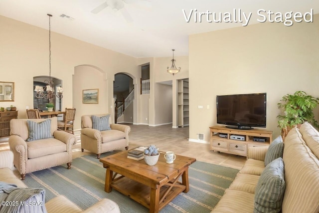 living area featuring vaulted ceiling, stairway, ceiling fan with notable chandelier, visible vents, and arched walkways