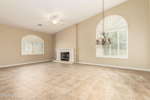 unfurnished living room with vaulted ceiling, a fireplace with raised hearth, baseboards, ceiling fan with notable chandelier, and visible vents
