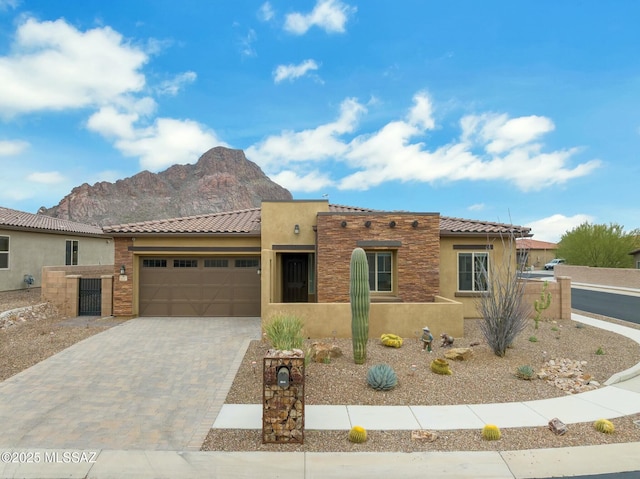 pueblo revival-style home featuring a tiled roof, decorative driveway, a mountain view, an attached garage, and stucco siding
