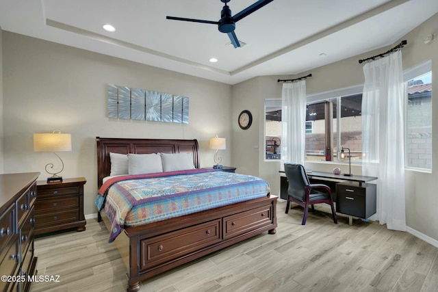 bedroom featuring light wood-style floors, a raised ceiling, baseboards, and multiple windows