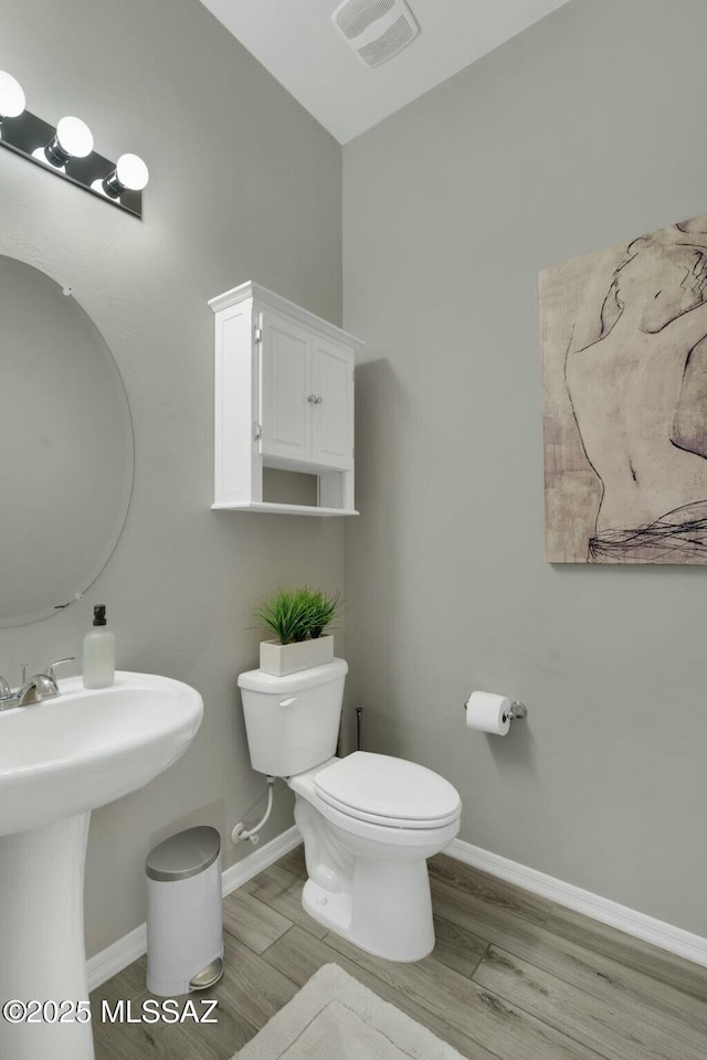 half bath with baseboards, toilet, wood finished floors, and visible vents