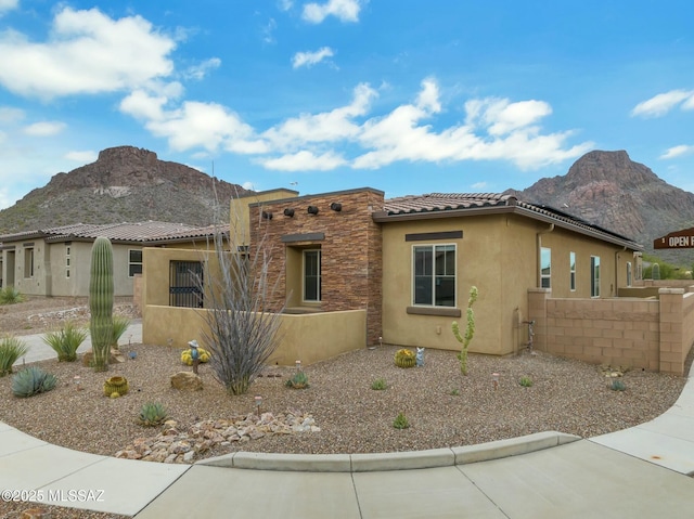 view of front of home with fence, a mountain view, stucco siding, and a tiled roof