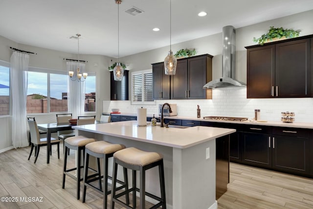 kitchen with a sink, stainless steel gas cooktop, a kitchen breakfast bar, light countertops, and wall chimney exhaust hood