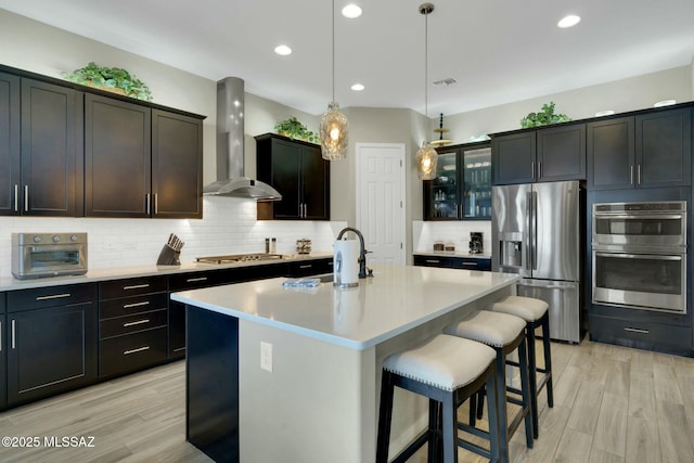 kitchen featuring wall chimney range hood, appliances with stainless steel finishes, a sink, a toaster, and light wood-type flooring