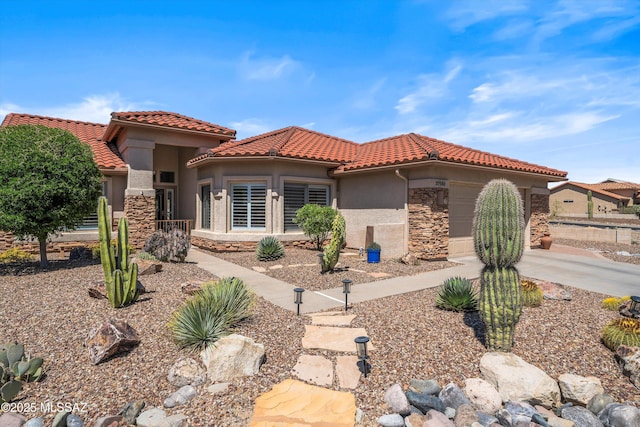 mediterranean / spanish house featuring an attached garage, a tiled roof, stucco siding, and stone siding