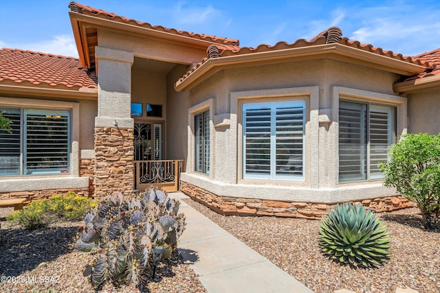 property entrance featuring a tiled roof, stone siding, and stucco siding
