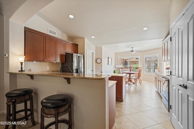 kitchen featuring stainless steel fridge with ice dispenser, visible vents, ceiling fan, a breakfast bar, and a peninsula