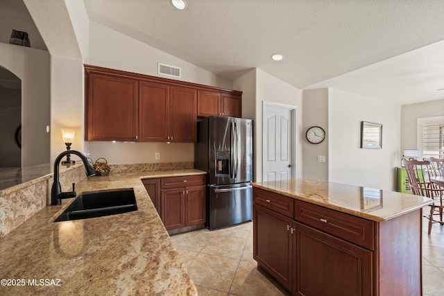 kitchen with visible vents, stainless steel fridge, a sink, vaulted ceiling, and light stone counters